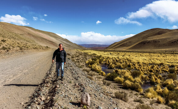 Male traveler walking on a remote dirt road next to a high-altitude wetland vega in the Andean Puna.