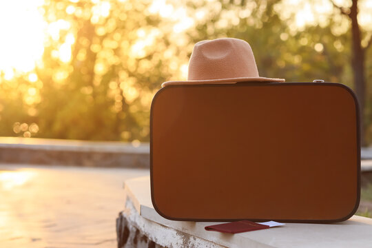 Suitcase with passport and hat on parapet in autumn park, closeup