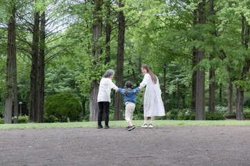 Fototapeta premium 春の新緑の公園で遊ぶおばあちゃんとお母さんと手を繋ぐ歩く寄り添う全身の後ろ姿顔無し 広角全身