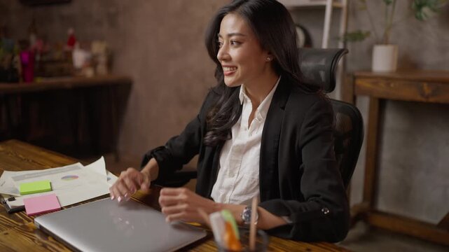 Business woman in office sitting in chair with laptop on desk, professional female working with paper and chart on wooden table, focused workspace planning document review and meeting focus