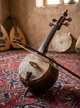 Traditional North African Rebab Fiddle with Bow on Berber Carpet in Ancient Mud-Wall Room with Oud and Frame Drum