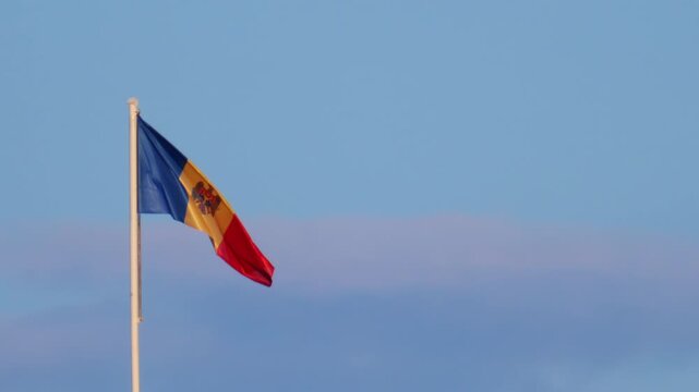 Moldovan national flag waving on a tall flagpole against a clear blue sky