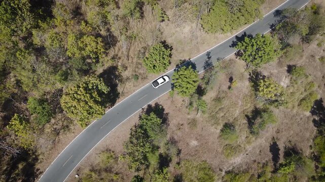 Aerial drone footage of a pickup truck driving on a rural road through countryside landscape. Scenic view of travel, transportation, and freedom in nature