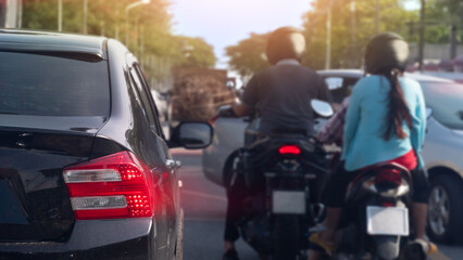 Street scene featuring two people on a motorcycle navigating through slow-moving car traffic. The image captures the mixed mode of transportation commonly found in busy metropolitan areas. © thongchainak