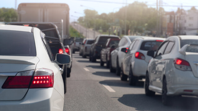 Long line of cars stuck in a traffic jam on a bright day. Perspective is from behind a white sedan. Showing the vast number of vehicles extending into the distance on a multi-lane road.