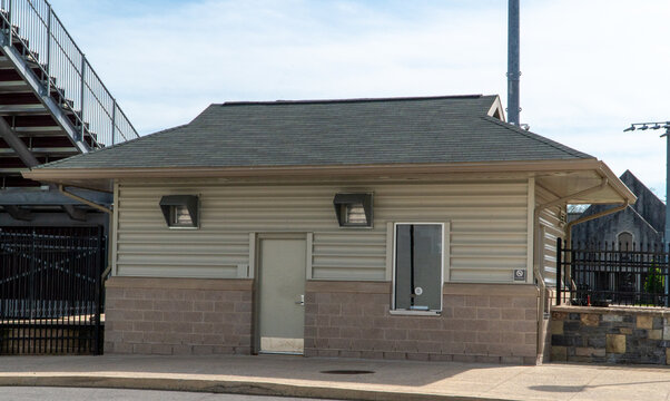 Exterior view of a beige and block building, likely a concession stand or ticket booth, at a sports stadium with bleachers, a light pole, and blue sky overhead, perfect for events and outdoor venues.