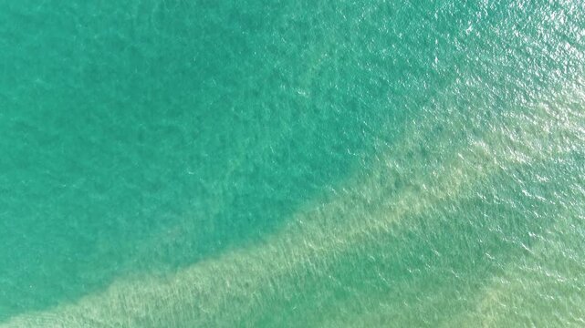Aerial view drone footage of clear turquoise sea water ripple surface with sandy bottom visible near tropical beach