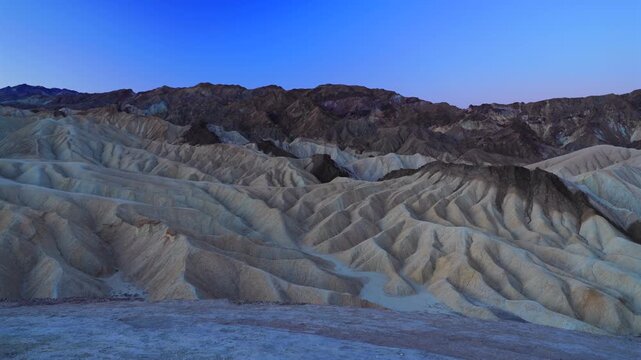 Dramatic eroded badlands and sedimentary rock formations at Zabriskie Point during blue hour twilight. Rugged desert terrain with deep ridges and valleys under gradient sky in Death Valley.