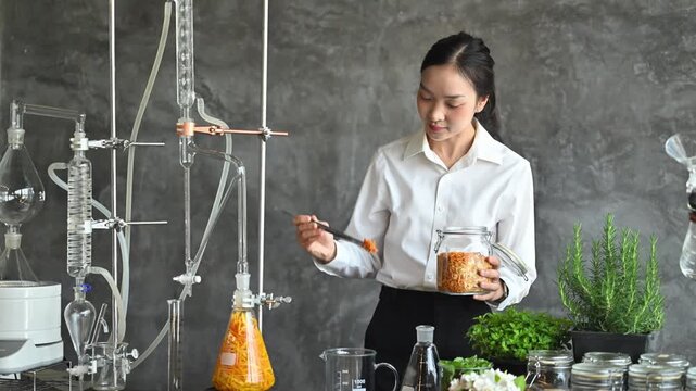 Young Asian Woman Scientist Formulating Natural Herbal Extract in Modern Laboratory with Fresh Botanicals and Distillation Equipment