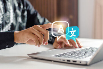 Businessman touching digital language translation icon on laptop keyboard at desk. Translation icon, symbolizing international trade, linguistic inclusivity, advanced machine learning © iqbal