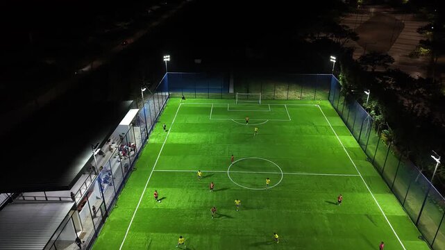 Aerial Drone View of Night Football Field with Players Training on Illuminated Artificial Turf