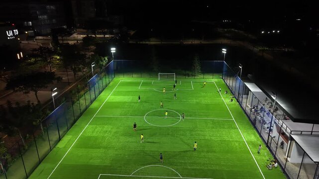 Aerial Drone View of Night Football Field with Players Training on Illuminated Artificial Turf