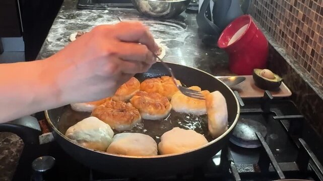 Balls of dough, with a ball inside, are fried in hot oil in a non-stick frying pan on the stove, gradually browning and rising, with bubbles forming around them. High quality FullHD footage