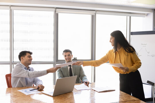 Smiling businesswoman handing out documents to clients or colleagues, sharing materials for reviewing infographics, statistics, and business data results during office corporate discussion meeting