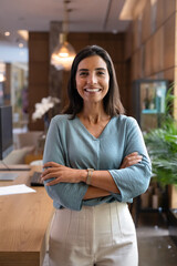 Portrait of Latina receptionist standing with arms crossed in hotel reception, ready to assisting...