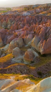 Vertical video. Goreme, Nevsehir, Turkey. Devrent Valley fairy chimneys and sculpted volcanic tuff formations glowing in warm golden hour light, aerial panoramic view over the vast eroded landscape. 