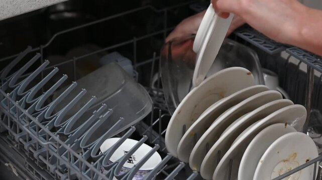 Hands loading dirty dishes into dishwasher rack for cleaning.