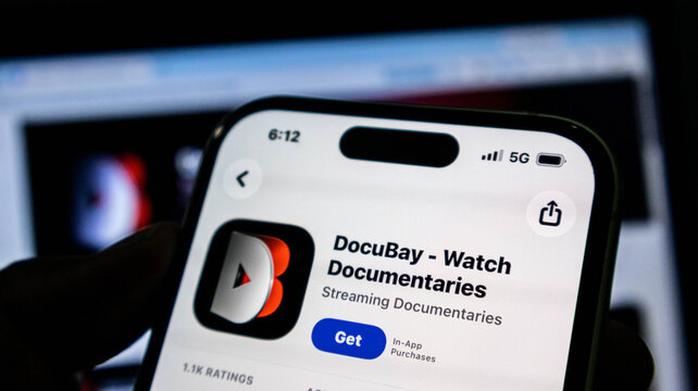 Closeup of a smartphone screen displaying the docubay documentary streaming app store page, held in a hand against a blurred background