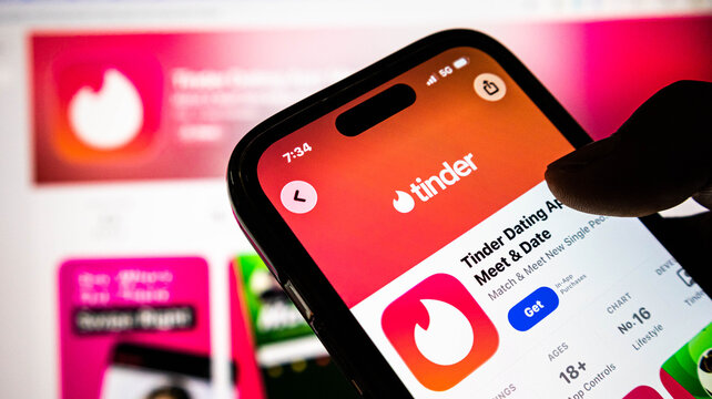 Closeup of a person holding a smartphone displaying the tinder dating app on the apple app store screen