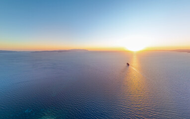 Obraz premium Kusadasi, Turkey - July 4, 2025: Panorama of cruise liner in pristine sea against sun creating glittering path on water. Majestic vessel sailing through golden sun glimmer at sunset. Aerial view.
