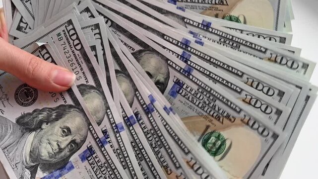 Close up slow motion of female hands counting numerous new one hundred dollar bills in a fan shape.