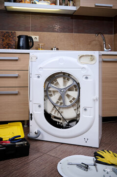 A set of professional tools against the background of a disassembled washing machine in the kitchen. Professional repair of household appliances.
