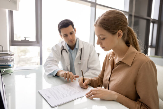 Woman patient signing contract sits at desk with professional physician points on medical consent terms, clarifying examination procedure, reviewing treatment agreement during consultation in clinic