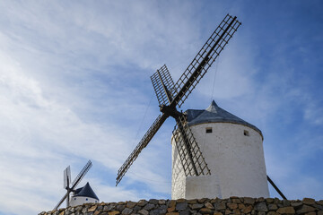 Naklejka premium Consuegra,Spain,White windmills with stone walls under a blue sky with scattered clouds