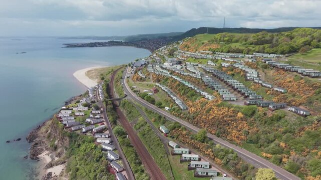 Aerial cinematic drone forward flyover shot of Pettycur Bay holiday caravan park on hillside and scenic coastline, Fife, Scotland.