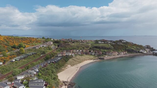 Aerial cinematic drone forward flyover shot of Pettycur Bay sandy beach, coastal holiday park, and seaside houses, Fife, Scotland.