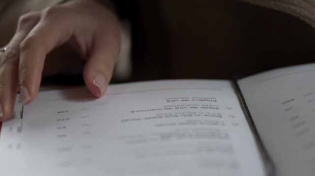 Close up on hands flipping through pages of a menu or book with blurred background.