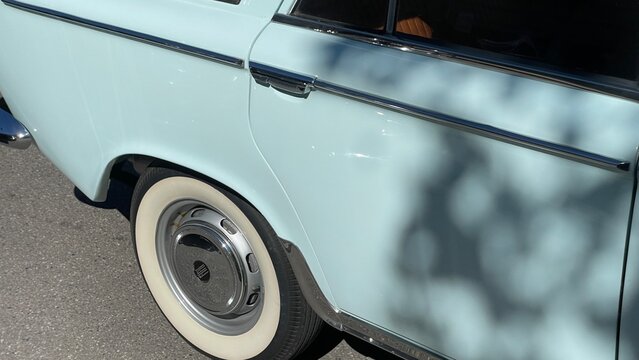 Retro Car Elegance: A close-up view of a vintage pale blue car, showcasing its distinctive chrome accents, whitewall tire, and a wheel cover, hinting at classic automotive design and nostalgia.