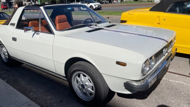 White Classic Sports Car with Targa Top: A pristine white classic sports car, featuring a distinctive targa top and sporty alloy wheels, parked outdoors under natural light.