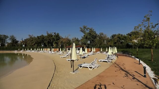 Walk along the shore of the city lake with a sunbathing beach and sun loungers. Sunny summer day