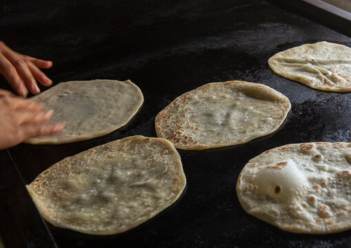 Manipulacion de alimentos, manos de mujer Mexicana haciendo tortillas de harina en un puebo de Mexico en un comal junto a una ventana, en Baja California Sur.