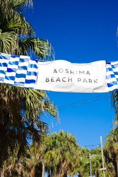 Aoshima Beach Park banner hanging between palm trees under blue sky.