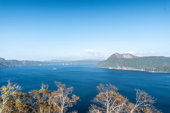 Scenic view of Lake Mashu with autumn foliage under a clear blue sky.