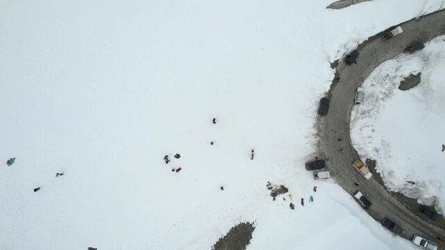 Aerial drone straight down rising shot of tourists exploring snowy mountains near Shinkula Top Pass and Sissu with parked 4X4 vehicles on winding roads in Ladakh Himachal Pradesh India during snowfall