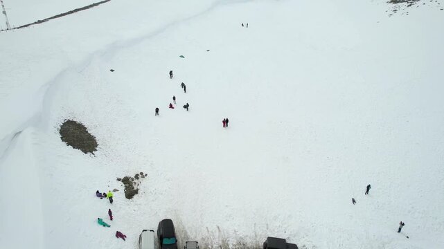 Aerial dronie shot flying away from people in snowy field to show 4X4 car bus parking on winding roads and snow covered mountains of Shinkula top pass in Sissu Ladakh Himachal Pradesh
