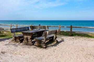 Fototapeta premium Wooden benches on the sand above a high bank. A magnificent view of the turquoise sea below. This photo was taken in beautiful, sunny weather. Blue sky above.