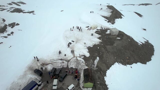 Aerial drone panning down to tourists climbing stairs to Sinkula Top hill surrounded by snow covered mountains with the 4X4 cars parked nearby showing the beauty of Ladakh Leh India