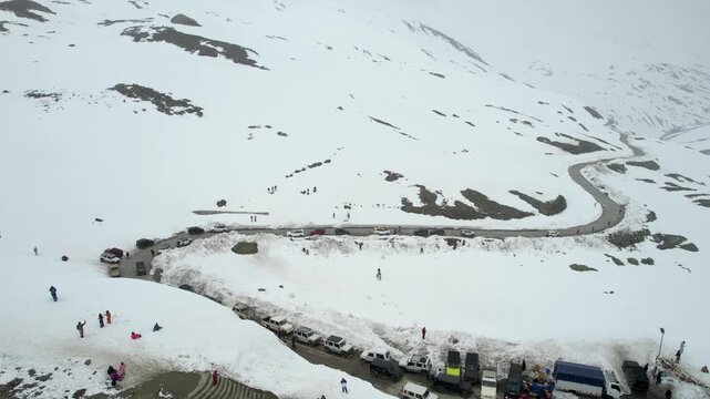 Aerial drone panning showing tourists enjoying snow amidst himalaya mountains with the Shingo La pass road winding off in the distance and 4X4 cars parked nearby showing the beauty of Ladakh Leh India