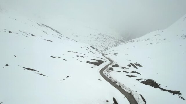 Aerial drone moving forward showing the Shingo La Pass road amid snow covered Himalaya mountains during snow fall showing the cold and beautiful environments of Ladakh, Leh, Sissu and Himachal Pradesh