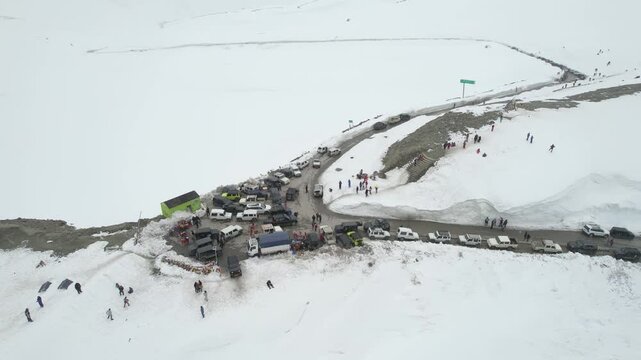 Aerial dronie shot flying away from crowd of people and 4X4 car bus parking to show snow covered surroundings winding roads and mountains of Shinkula top pass in Sissu Ladakh Himachal Pradesh