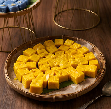 Malaysian Kueh Talam, cut into cubes and presented on traditional woven bamboo trays with banana leaves, resting on a dark wood surface with elegant lighting.