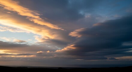Fototapeta premium Golden sunset clouds over a dark landscape horizon at twilight