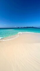 Fototapeta premium Turquoise ocean waves lapping on a white sand beach under a clear blue sky