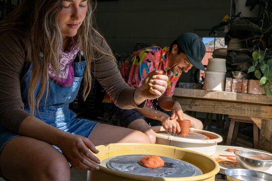 Young woman and man spinning wet clay on pottery wheels