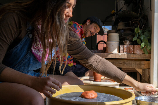 Young woman and man spinning clay on pottery wheels