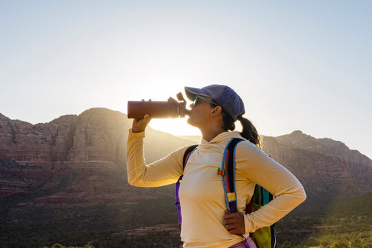 Female hiker drinks from water bottle backlit sunburst